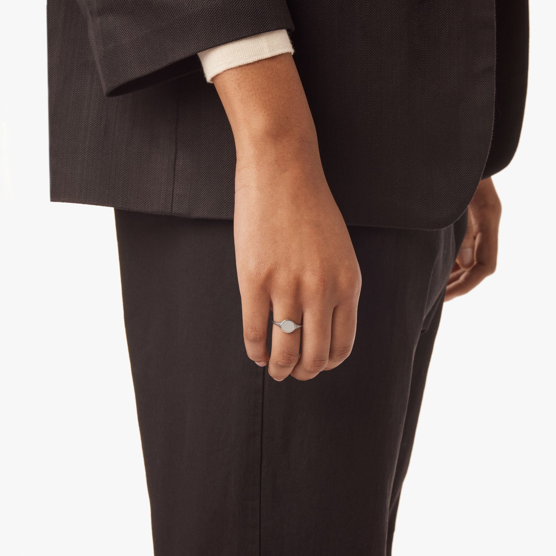 A person in a black suit and white shirt is shown from the waist down, their left hand relaxed by their side and wearing Shinola’s Petite Round Signet Ring - Sterling Silver for a timeless touch.