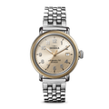 A Shinola Runwell Coin Edge Watch with a silver bracelet, gold bezel, cream dial, silver markers, and displaying 10:06. The watch face reads “Shinola Argonite-715 Detroit.”.