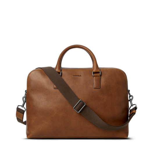 Shinola Double Zip Briefcase in medium brown leather with top handles and a dark brown adjustable, detachable shoulder strap, shown on a plain white background.