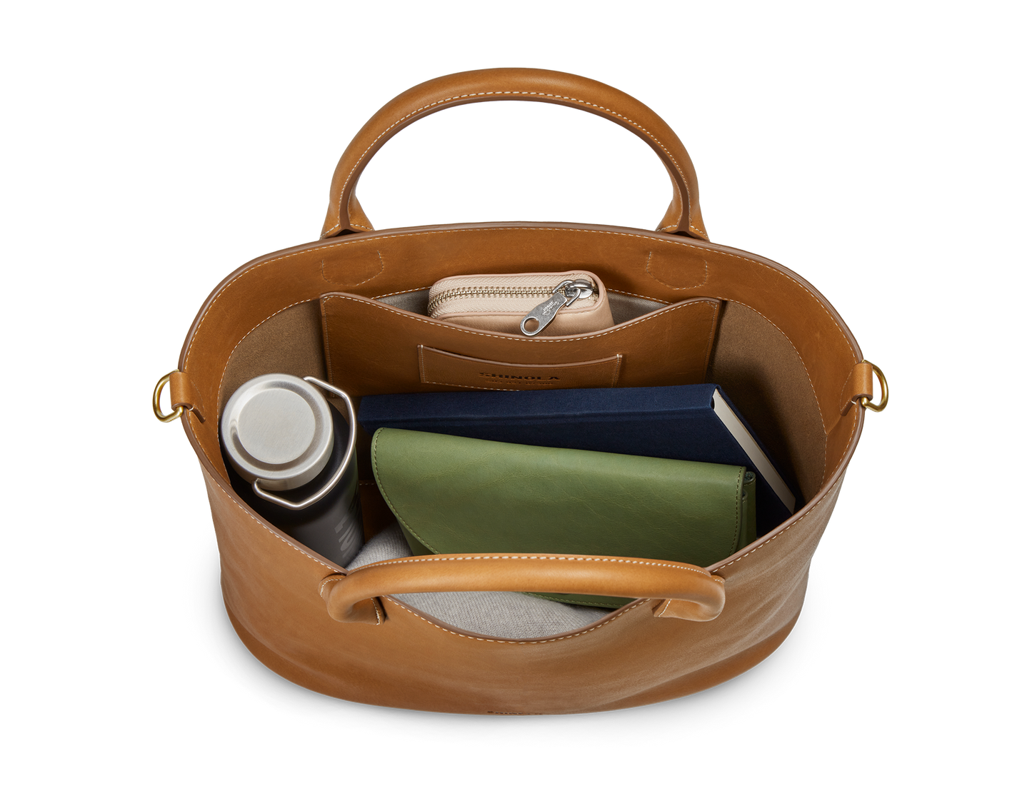Top view of the Shinola 12 Hour Tote Bag in tan, displaying its roomy interior pocket neatly storing a silver water bottle, green wallet, navy notebook, and beige pouch—ideal for carrying your daily essentials.