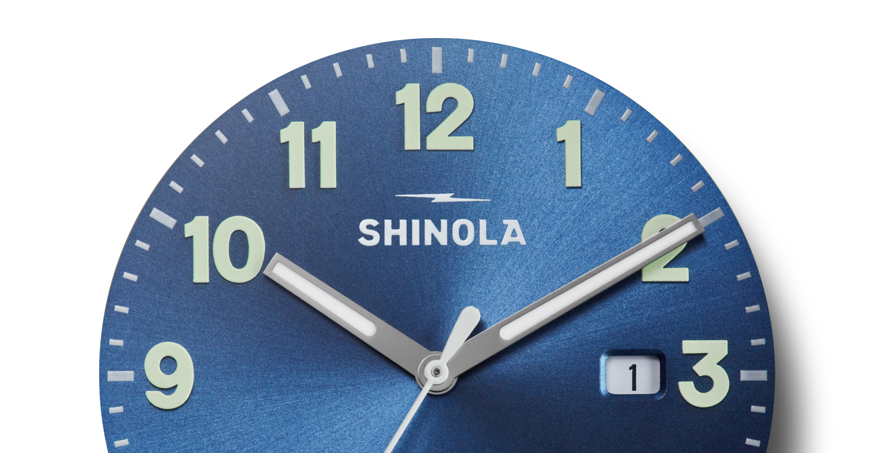 Close-up of a Shinola Detrola Watch - Denim Blue shows the time as 2:08. The watch features large, luminous numbers and hands, and a date window showing "1" next to the 3 o’clock position.
