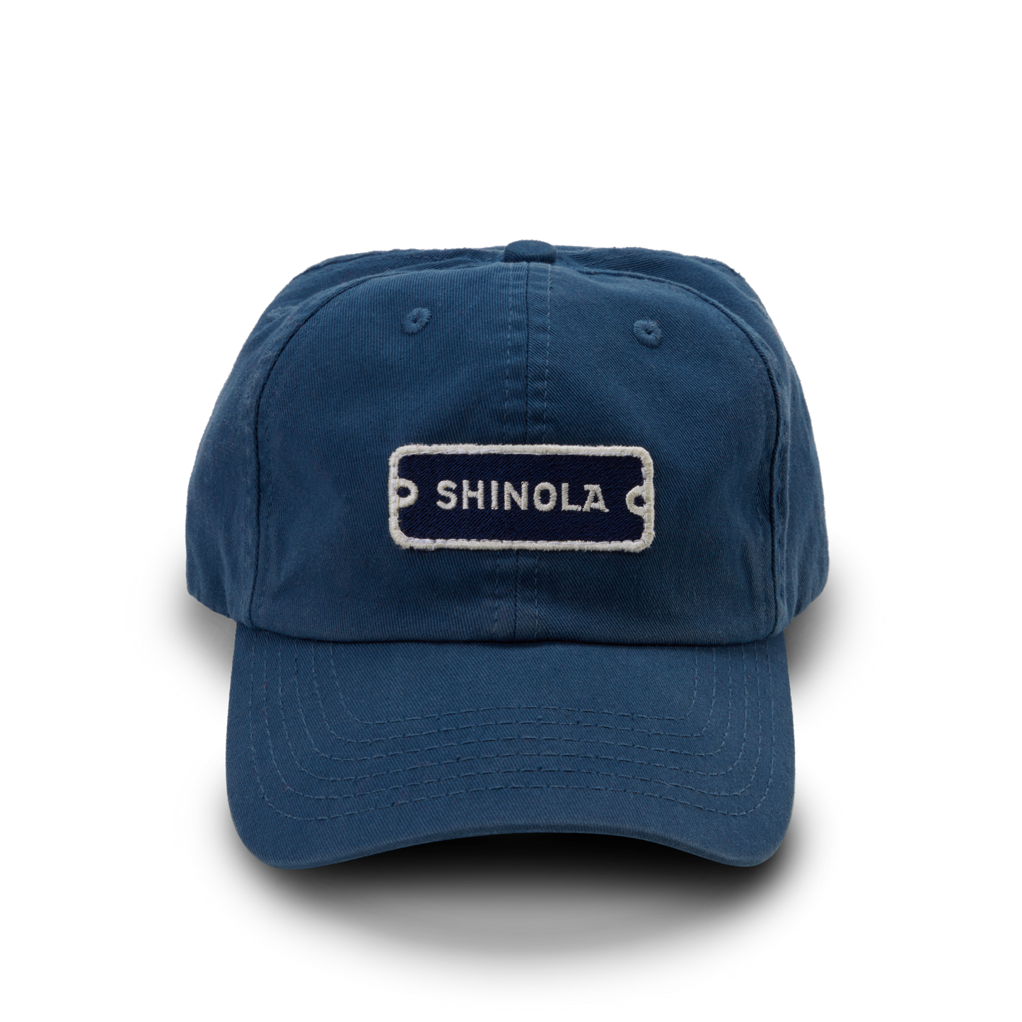 The Shinola Cotton Twill 6 Panel Cap is crafted from garment-dyed cotton twill in blue, featuring a white-stitched SHINOLA patch, visible stitching, curved brim, and a leather strap closure.