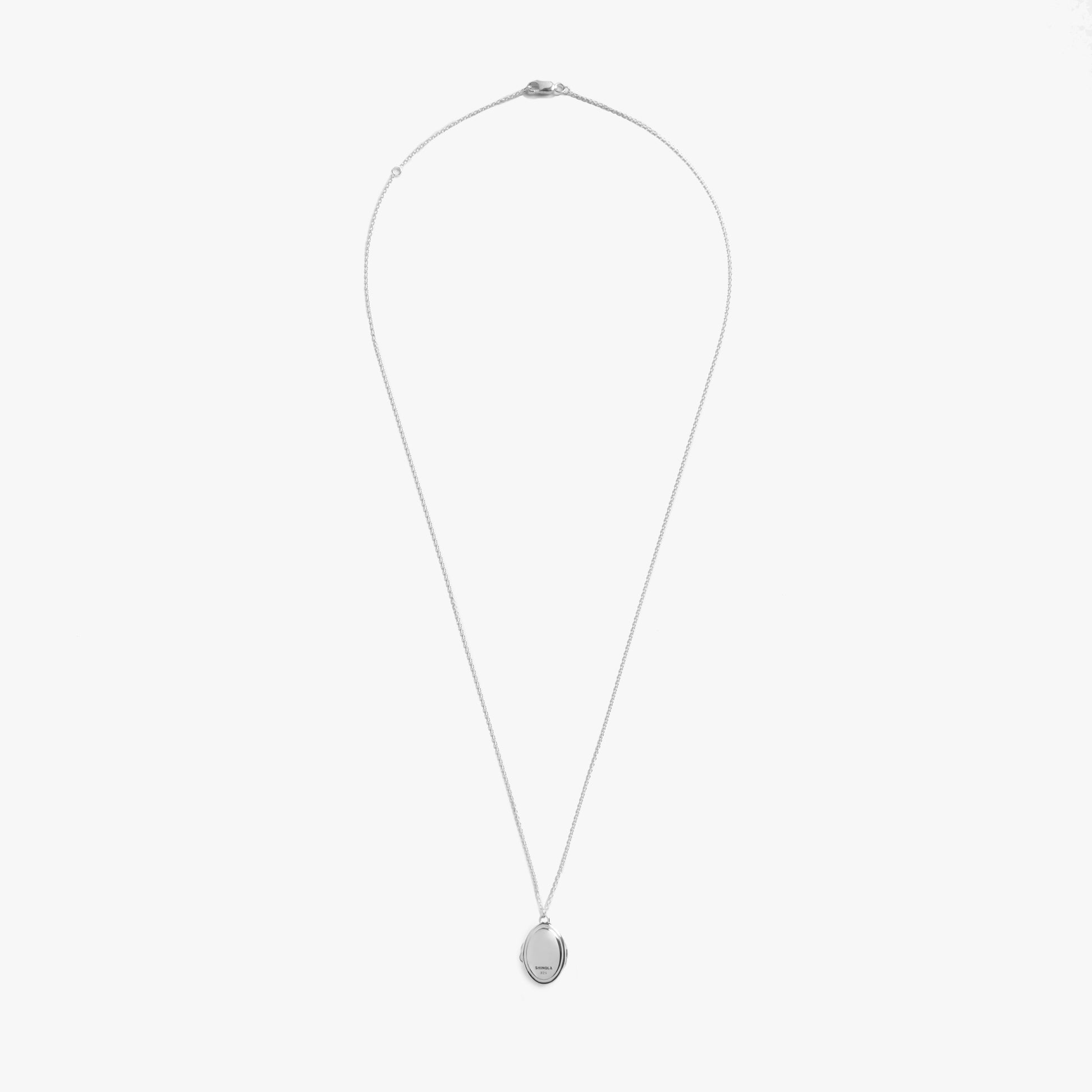 The Shinola Heirloom Petite Locket Necklace in sterling silver features a thin chain and small oval pendant, ideal for engraving, shown against a plain white background.