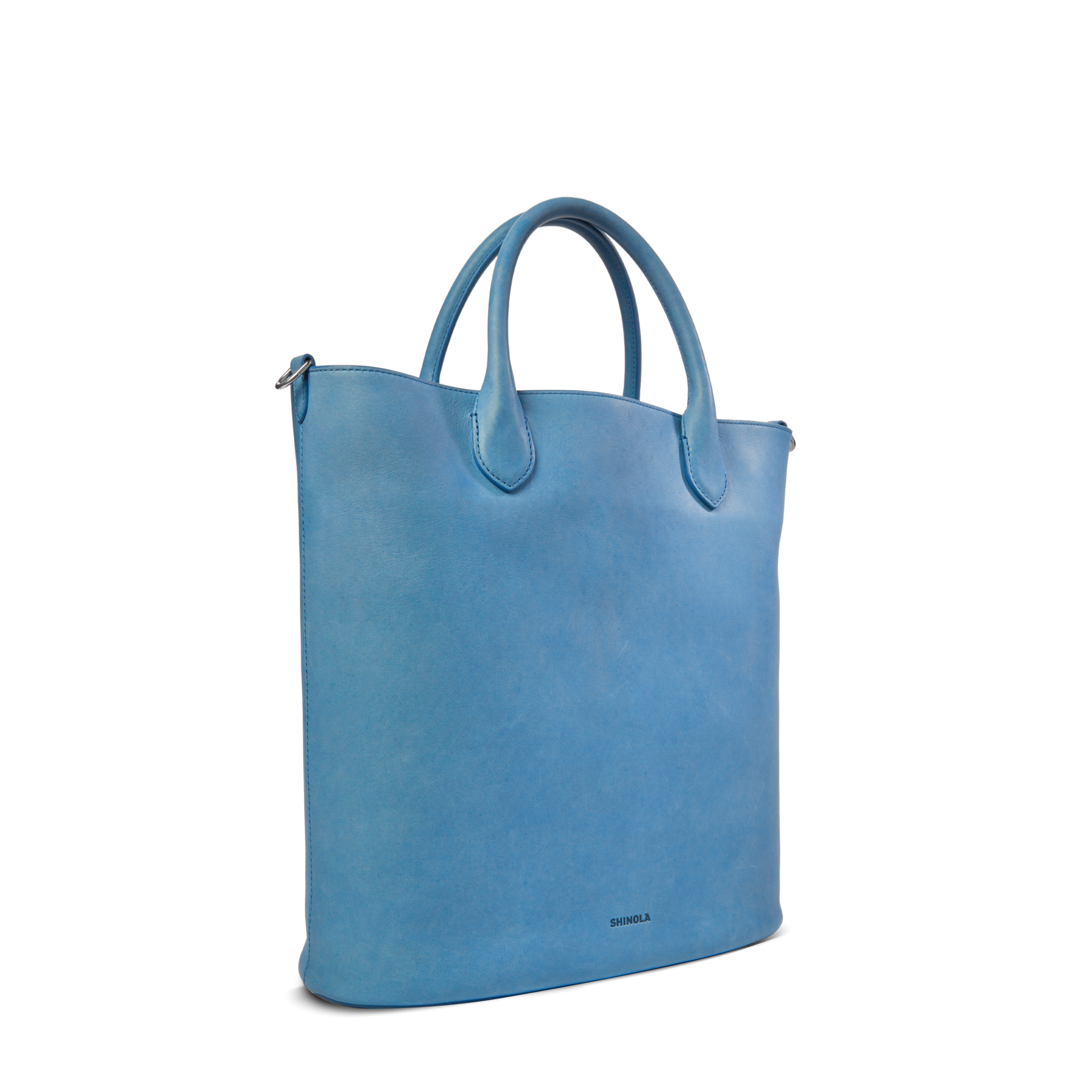 The Shinola 12 Hour Tote Bag - River stands upright on a white background, featuring light blue smooth natural leather, two rounded handles, and subtle branding near the bottom.