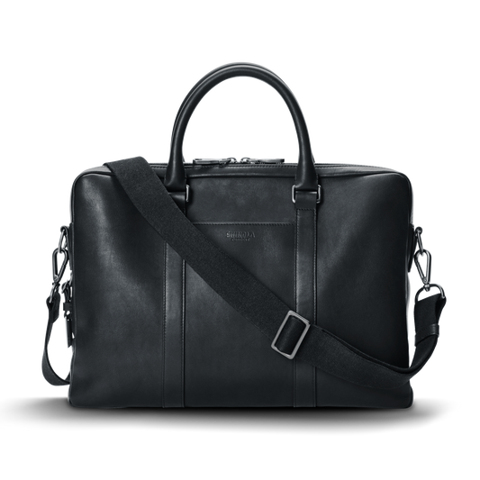 A shinola.momputer Briefcase in black, featuring dual top handles, a detachable shoulder strap, and subtle stitching details, set against a plain white background.
