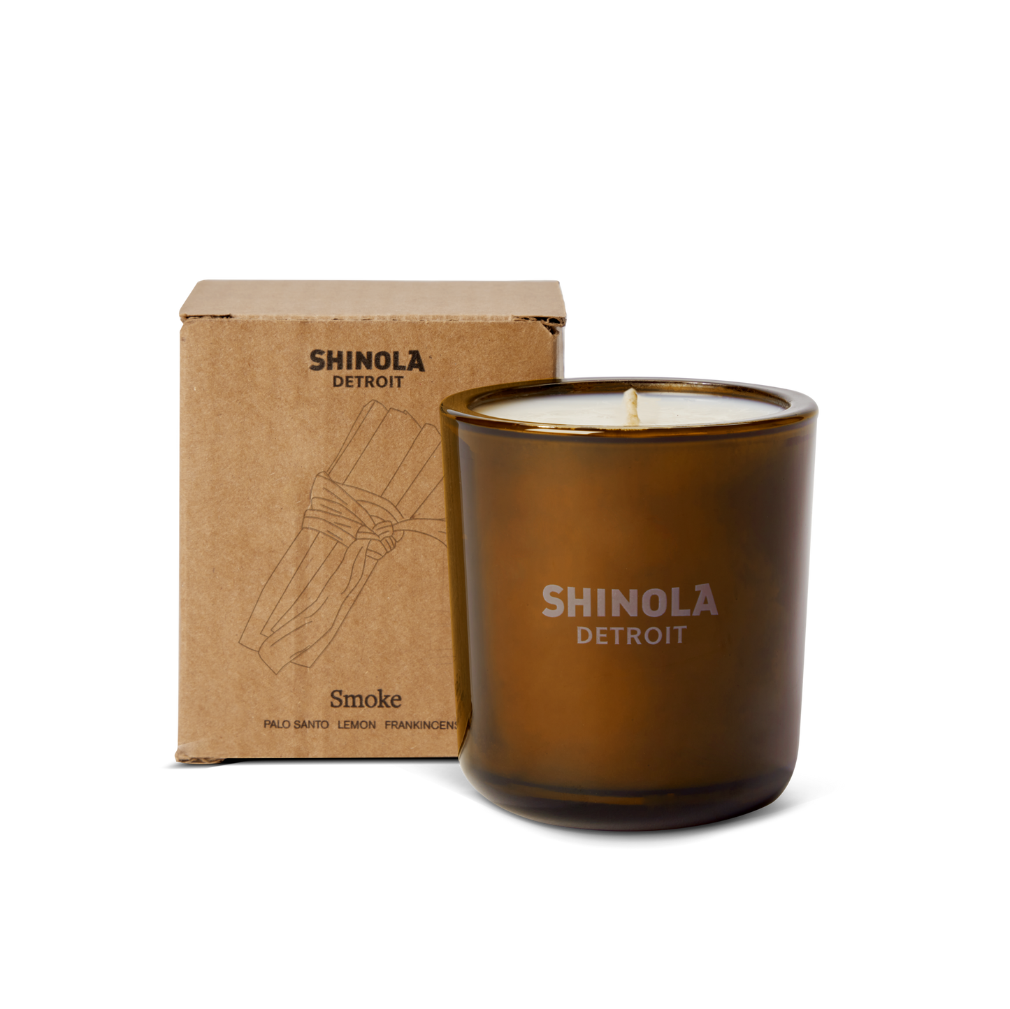 A brown 8oz Shinola Smoke Scented Candle sits in front of its illustrated box; this Detroit fall candle features a woody blend of Palo Santo, Lemon, and Frankincense, crafted with coconut soy wax.