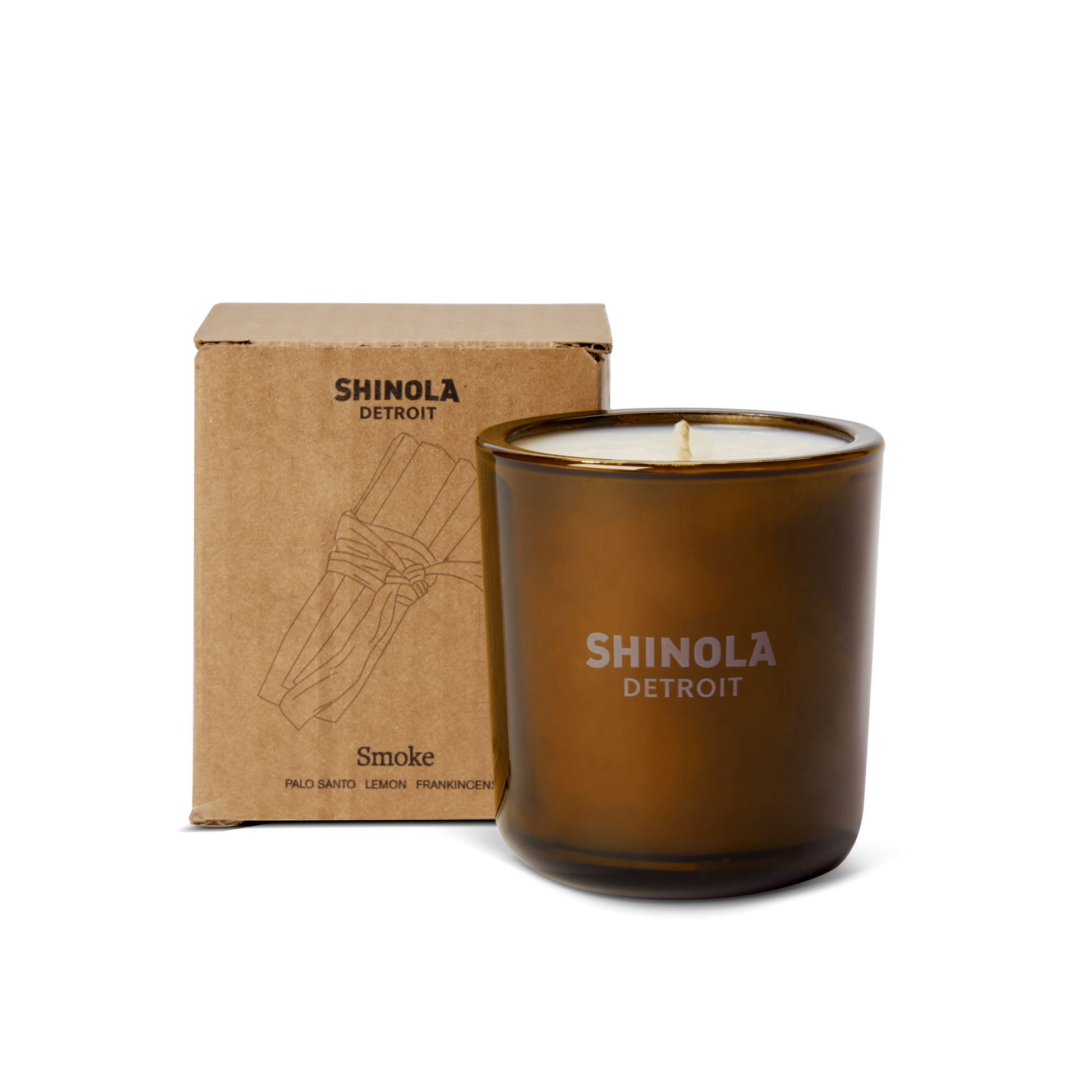 A brown 8oz Shinola Smoke Scented Candle sits in front of its illustrated box; this Detroit fall candle features a woody blend of Palo Santo, Lemon, and Frankincense, crafted with coconut soy wax.