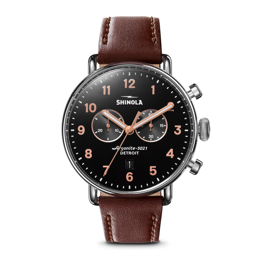 The Shinola Canfield 2 Eye Chrono - Black features a black dial, rose gold hands and numbers, two subdials, date window, brown leather strap, stainless steel silver case, and two buttons on the right side.