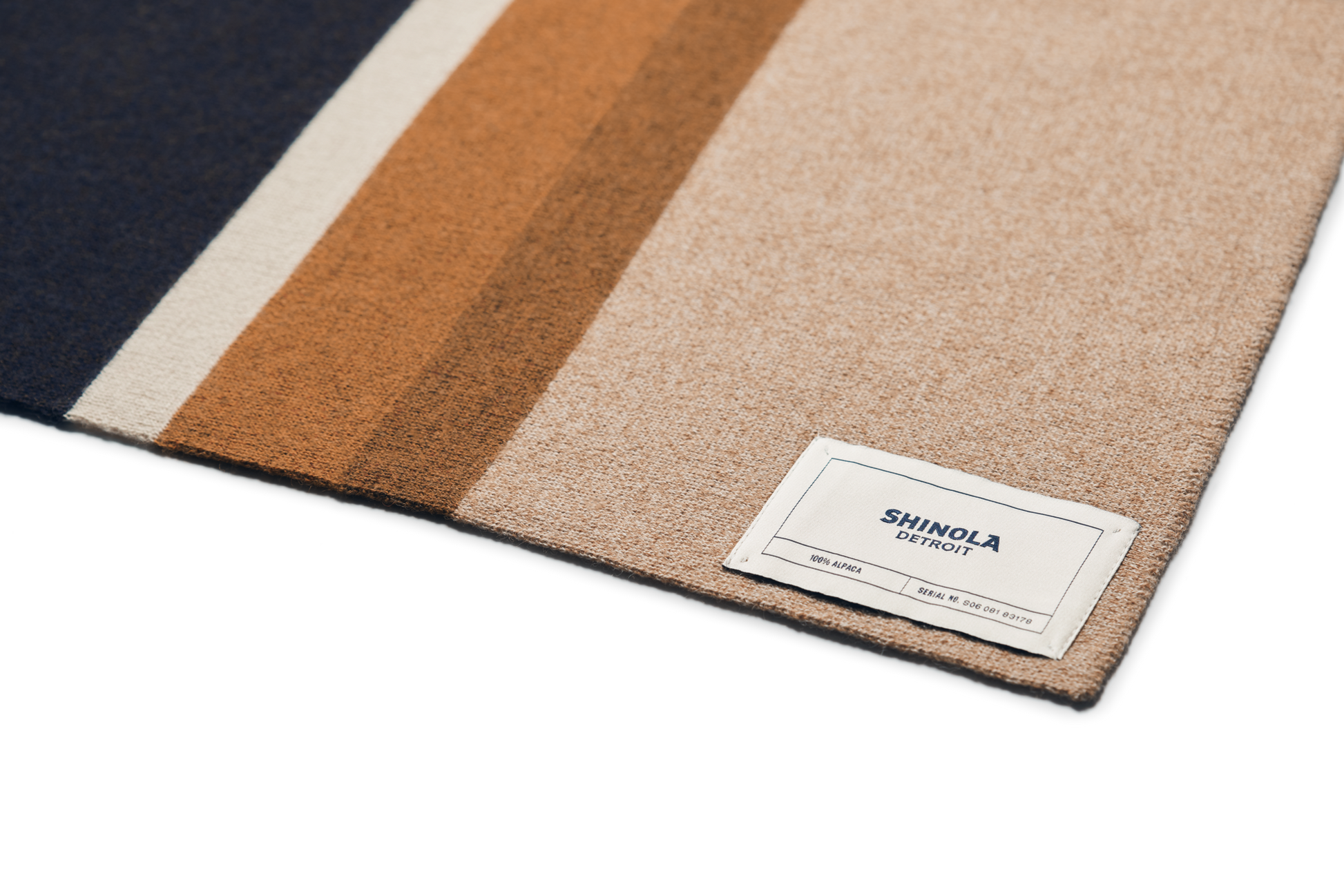 A close-up of a Shinola Alpaca Throw Blanket in pink and beige stripes, featuring a white Shinola label in the corner.