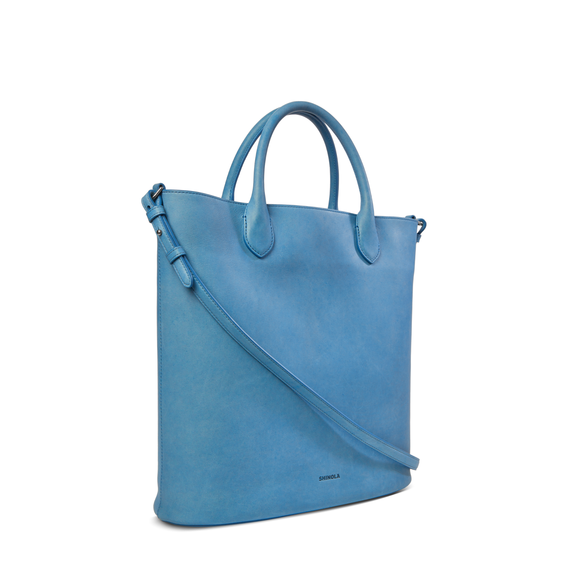 The Shinola 12 Hour Tote Bag - River is a stylish, light blue natural leather tote with short handles and a long adjustable strap—perfect for everyday use—shown against a plain white background.