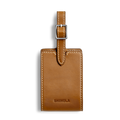 The Shinola Luggage Tag - Tan is crafted from Italian leather with white stitching, a silver buckle strap, and the Shinola logo embossed on the front, ideal for monogramming and shown against a plain white background.