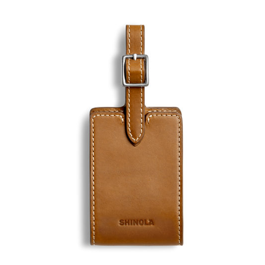 The Shinola Luggage Tag - Tan is crafted from Italian leather with white stitching, a silver buckle strap, and the Shinola logo embossed on the front, ideal for monogramming and shown against a plain white background.