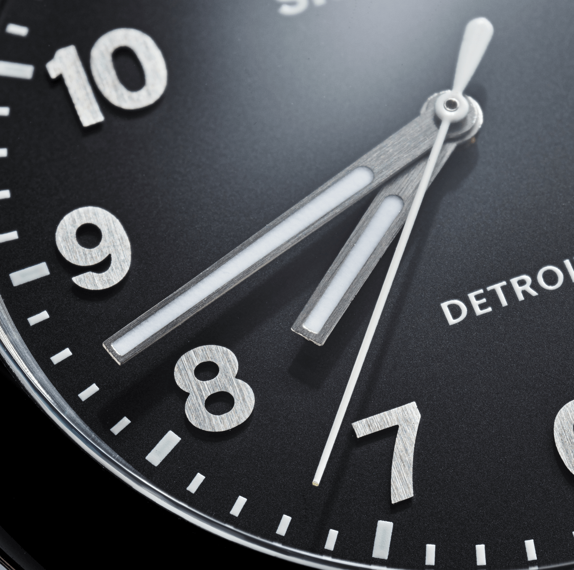 Close-up of a Shinola Detrola Watch - Black face showing numbers 7 to 10, with the hour hand at 8 and minute hand at 9. The partially visible logo highlights its classic American style and Shinola’s reputation for durability.