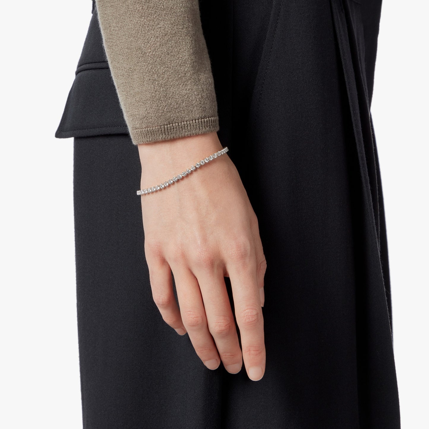 A close-up of a hand and wrist wearing the Shinola 3 Carat 7" Diamond Tennis Bracelet in white gold, styled with a black skirt or dress and a taupe long-sleeve top.
