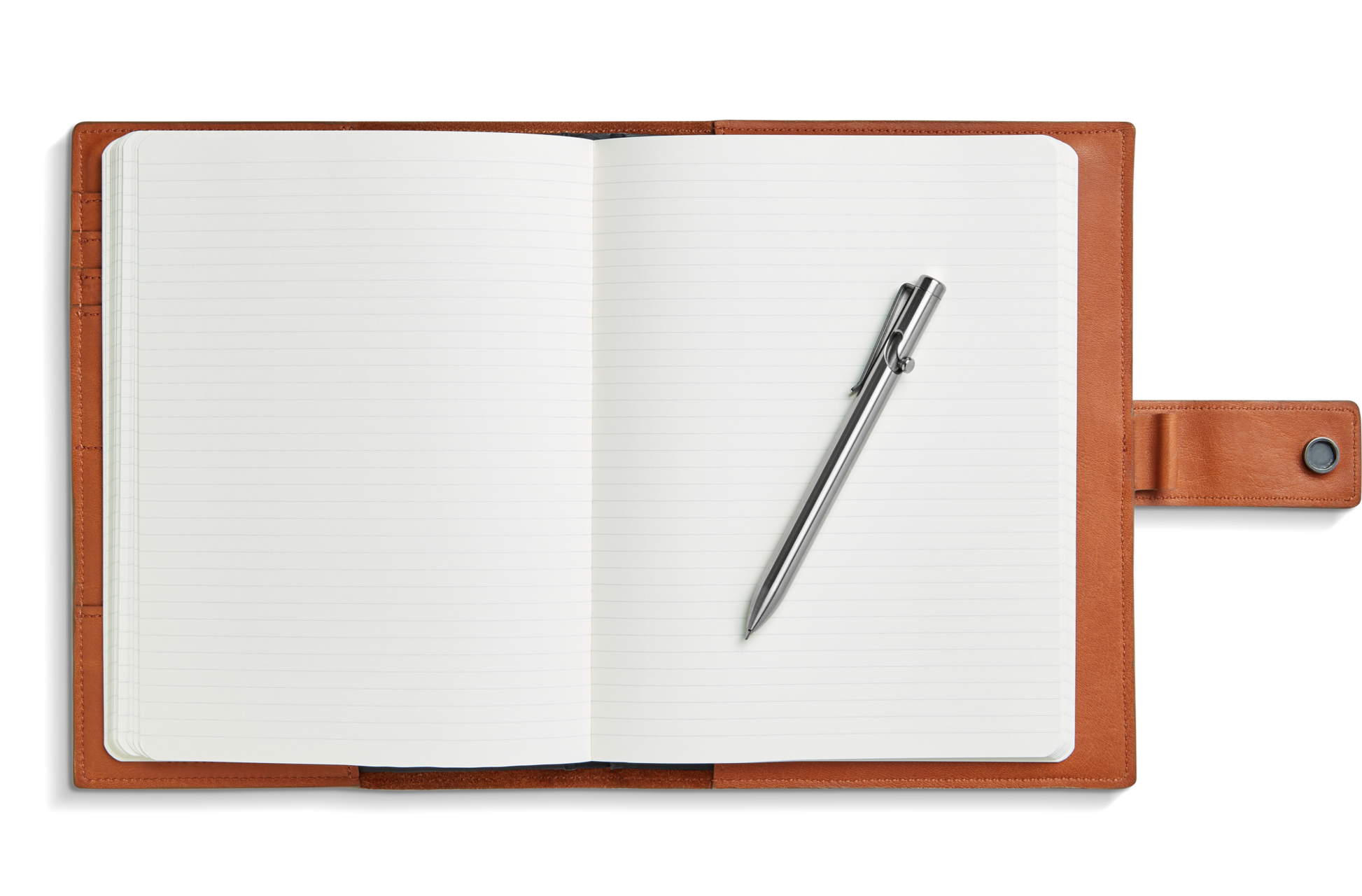 A Shinola open lined notebook with a brown leather cover lies flat, secured by a strap and button closure, with a Tactile Turn Titanium Bolt Action Pen in titanium finish resting diagonally on the right page.