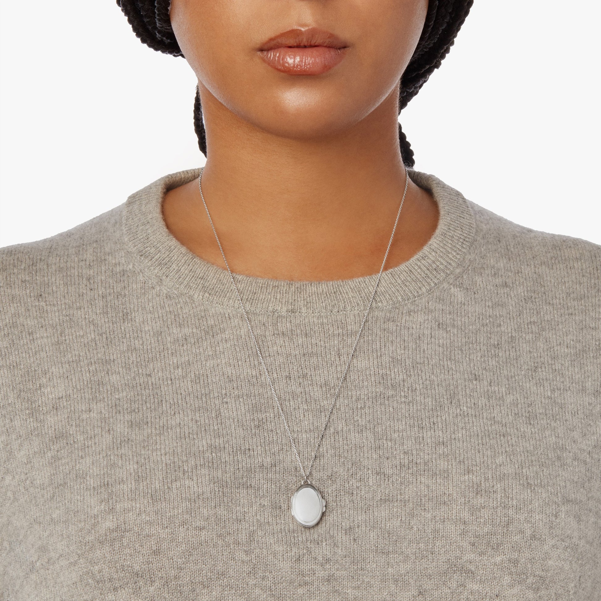 A woman models the Shinola Heirloom Statement Locket Necklace in sterling silver, paired with a light grey knit sweater, shown from the shoulders to above the lips against a plain white background.