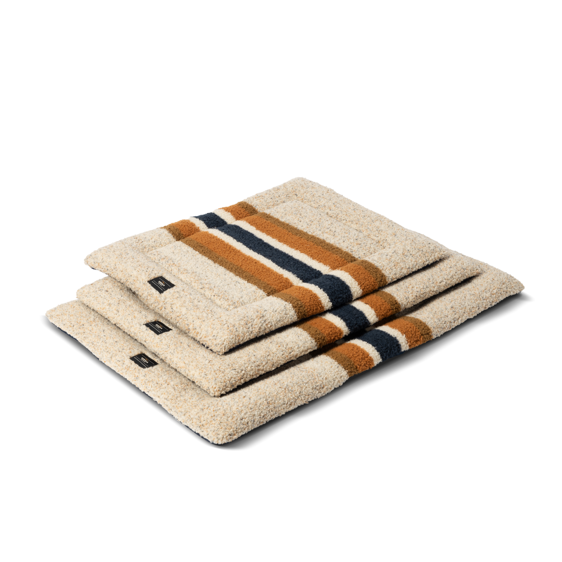 Three folded Crate Comfort Mat - Oat Stripe dog mats by Shinola, featuring beige with navy blue and brown stripes, are stacked atop each other against a plain white background.