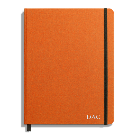 The Shinola Large Hard Ruled Journal in Bold Orange features a black elastic band, ribbon bookmark, and DAC initials in white at the bottom right. Crafted with acid-free paper for lasting notes.