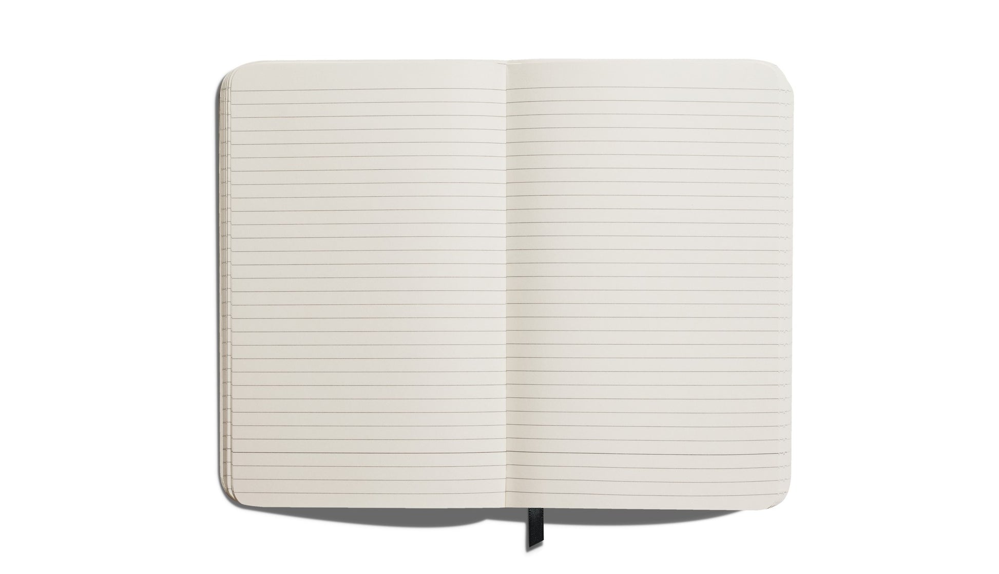The Shinola Medium Hard Ruled Journal in black features an open, blank, lined interior with rounded corners, a black ribbon bookmark, and smyth-sewn binding, photographed from above on a white background.