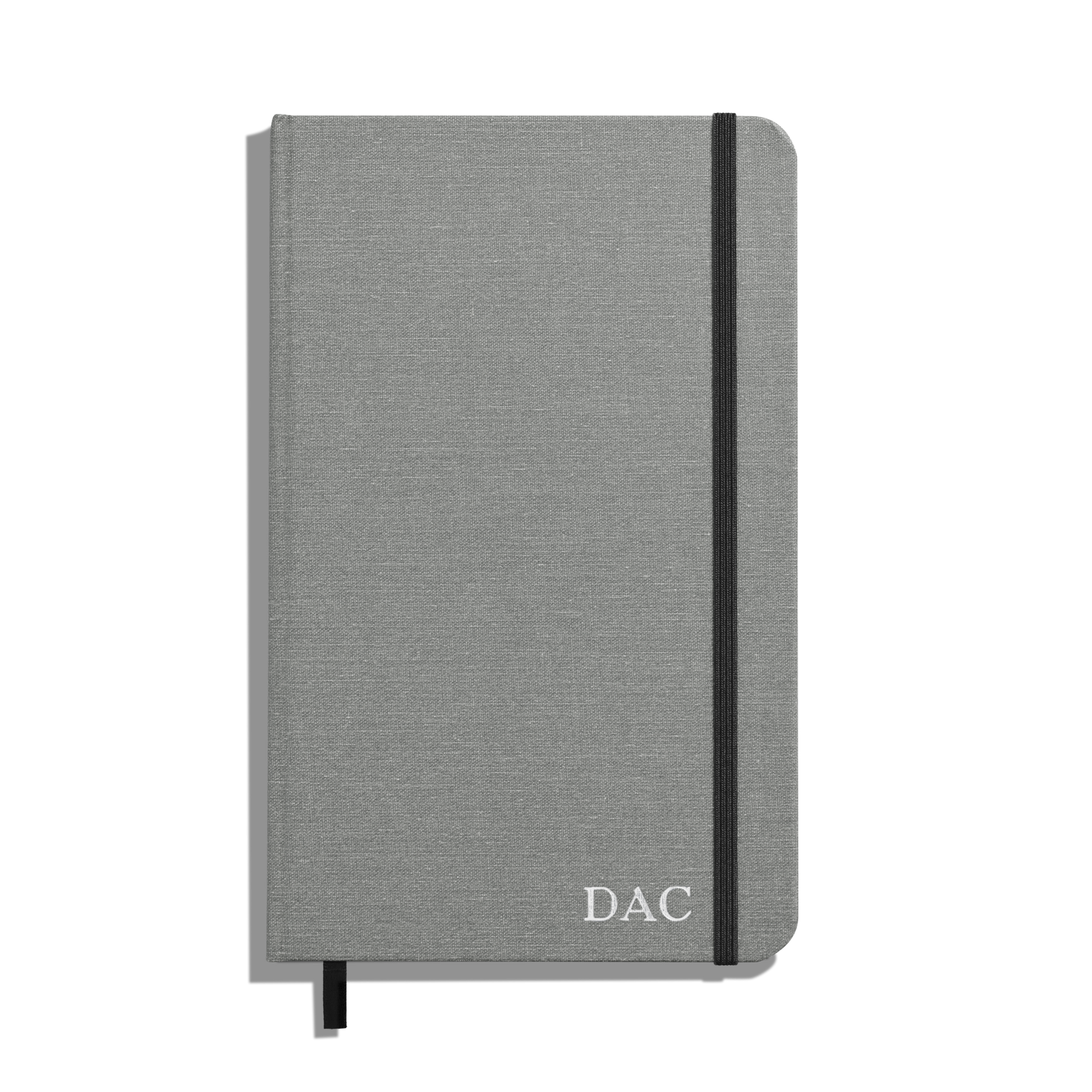 The Shinola Medium Hard Ruled Journal - Stone features a gray hardcover, smyth-sewn binding, black elastic band and ribbon bookmark, with DAC initials in white on the lower right corner of the cover.