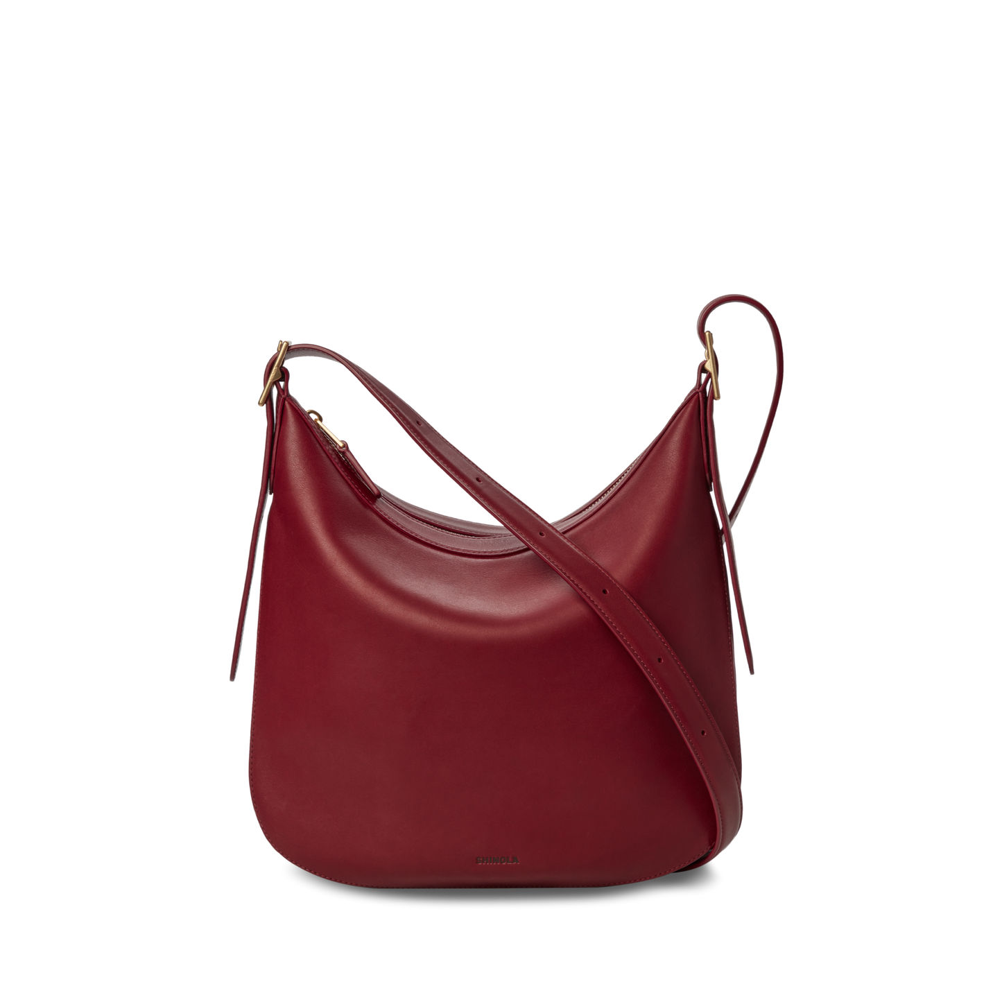 The Shinola Medium Bixby Crossbody - Ruby features natural leather in a curved, crescent shape with gold-tone hardware and an adjustable strap. This versatile shoulder bag is shown against a plain white background.