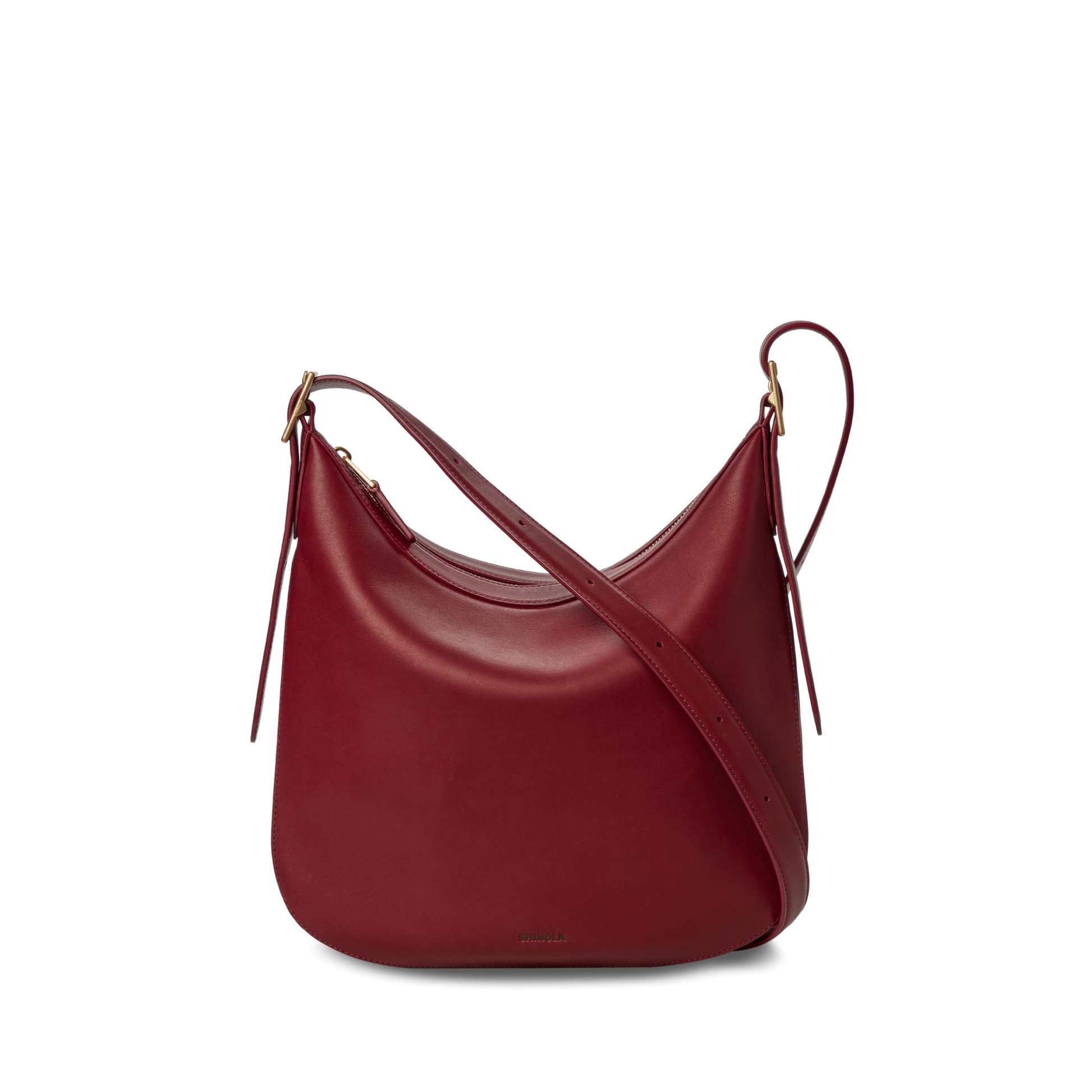 The Shinola Medium Bixby Crossbody - Ruby features natural leather in a curved, crescent shape with gold-tone hardware and an adjustable strap. This versatile shoulder bag is shown against a plain white background.